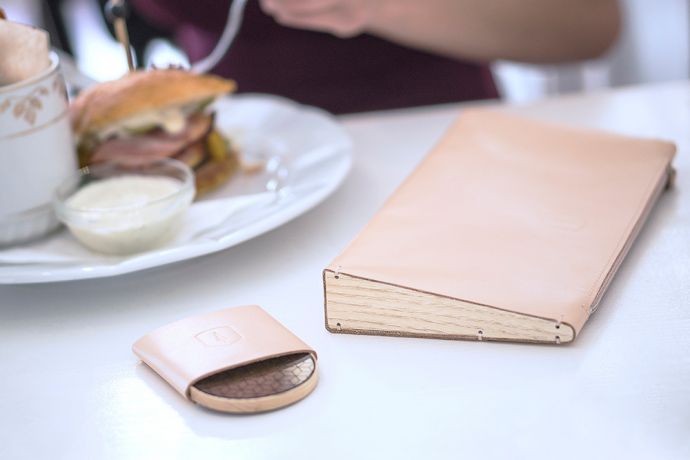 Die Lux Clutch Handtasche aus Leder mit Holzdetail und Holzspiegel Liti in einem Restaurant auf dem Tisch 