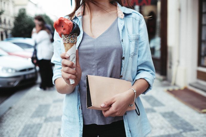 Eine Frau in einem blauen Hemd hält ein Eis und die Vespa Clutch Handtasche aus Leder mit Holzdetail