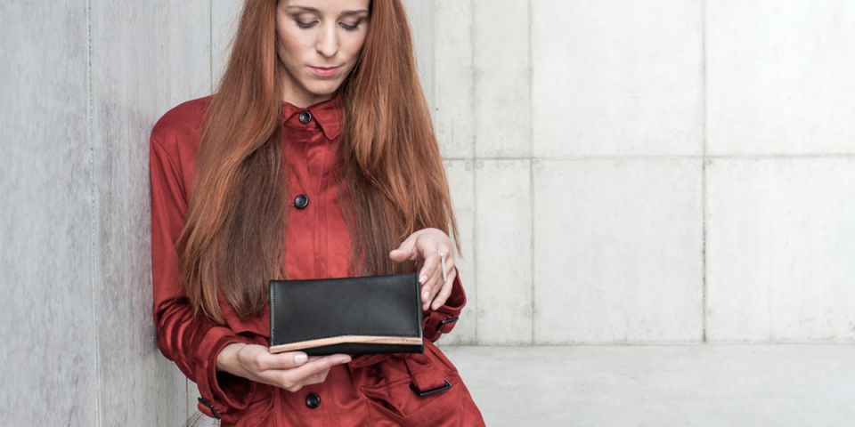 Eine Frau mit roten Haaren in einem orangefarbenen Mantel hält eine Geldbörse aus Holz und Leder Api Woman Wallet