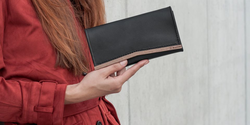 Eine Frau mit roten Haaren in einem orangefarbenen Mantel hält eine Geldbörse aus Holz und Leder Caleo Woman Wallet