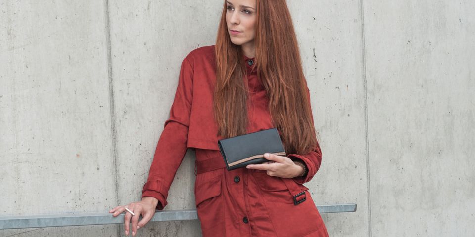 Eine Frau mit roten Haaren in einem orangefarbenen Mantel hält eine Geldbörse aus Holz und Leder Caleo Woman Wallet