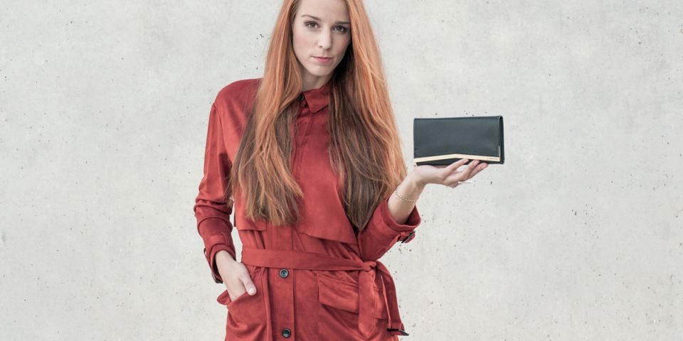 BeWooden - Eine Frau mit roten Haaren in einem orangefarbenen Mantel hält eine Geldbörse aus Holz und Leder Liti Woman Wallet