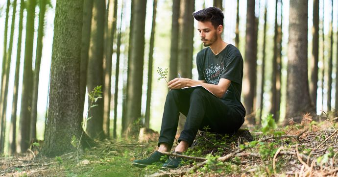 Ein Mann sitzt in einem Wald und schreibt in sein BeWooden Notizbuch