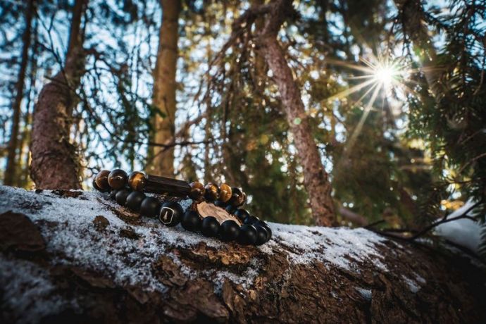 Ein BeWooden-Armband aus edlem Holz mit Steinen liegt auf einem schneebedeckten Ast im Wald 